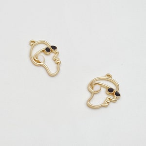 image shows two outline face charms in shiny gold tone metal, the face has a sunglasses detail and a hoop for attachment