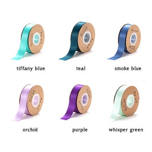 Puede incluir: Seis carretes de cinta de satén en varios colores: azul verdoso, azul Tiffany, azul humo, orquídea, morado y verde claro. Cada carrete tiene una etiqueta marrón con la palabra "ECCAIL" impresa.