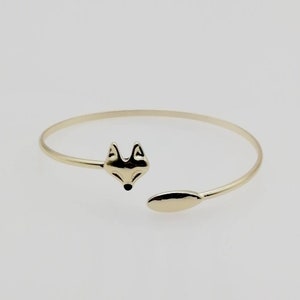 Könnte beinhalten: Ein goldfarbenes Armband mit einem Fuchs-Kopf-Anhänger. Das Armband ist offen und hat an einem Ende einen Fuchs-Kopf-Anhänger und am anderen Ende einen kleinen ovalen Anhänger.