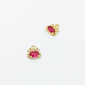 May include: Two gold-tone charms featuring red oval-shaped stones and clear rhinestones. The charms are shaped like a crab.