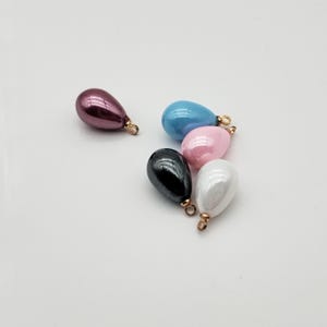 May include: Five pearlescent teardrop-shaped beads with gold-colored loops. The beads are in the colors pink, white, blue, black, and burgundy.