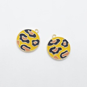 May include: Two gold-coloured metal charms featuring a leopard print design. The charms are round and have a hole at the top for attaching to a necklace or bracelet.