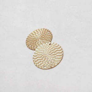 Könnte beinhalten: Zwei goldfarbene Metallkreise mit einer strukturierten Oberfläche und Löchern zum Aufhängen. Die Kreise überlappen sich leicht.