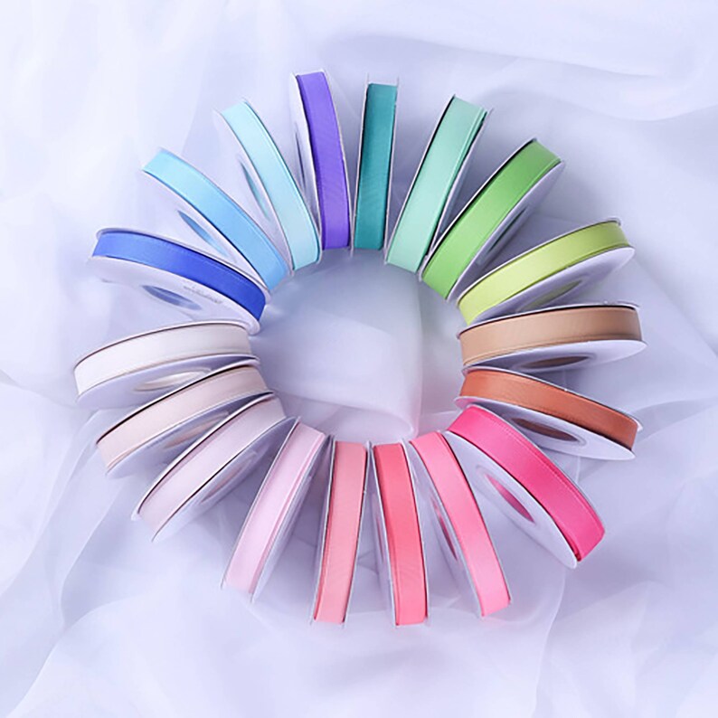 May include: A collection of 18 spools of ribbon in various pastel colors, including pink, blue, green, and purple. The spools are arranged in a circle on a white background.