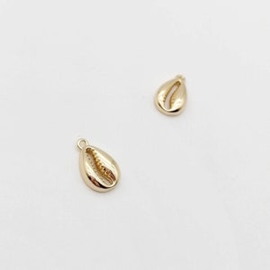 May include: Two gold-coloured shell charms, each with a detailed design, ideal for jewellery making or crafting projects.