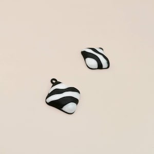 May include: Two black and white striped diamond-shaped charms with a shiny finish.