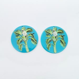 May include: Two round, turquoise blue, resin earrings with a white monkey sitting in a green palm tree.