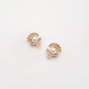 May include: Two gold-tone metal clam shell charms with a white pearl inside. Each charm has a loop for attaching to jewellery.