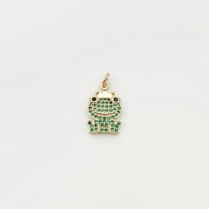 May include: A gold-tone charm in the shape of a frog, with green and black cubic zirconia stones.