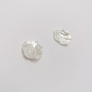May include: A pair of white pearl shell earrings. The earrings are shaped like a seashell and have a smooth, glossy finish.