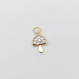 Puede incluir: Un charm de hongo dorado con detalles de cristal transparente. El charm tiene un bucle en la parte superior para sujetarlo a un collar o pulsera.