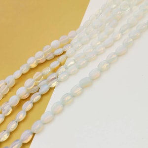 Puede incluir: Cadenas de cuentas ovaladas y opalescentes. Las cuentas son de color blanco nacarado con sutiles tonos iridiscentes. Las cuentas están dispuestas en líneas paralelas sobre un fondo blanco y dorado. Ideal para la fabricación de joyas.