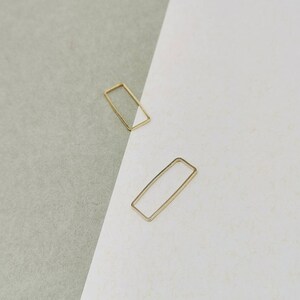 Può includere: Due anelli rettangolari in metallo color oro. Gli anelli sono su una superficie bianca e grigia.