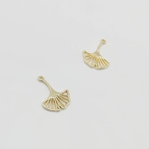 May include: Two gold-colored metal ginkgo leaf charms with a loop at the top for attaching to jewelry or other crafts.