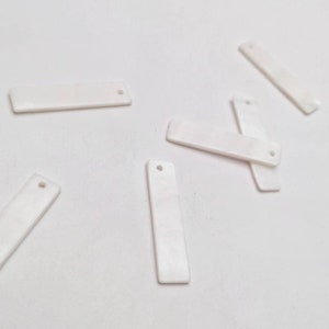 May include: A group of six white rectangular pieces of material with a hole in the center of each piece. The pieces are arranged on a white surface.