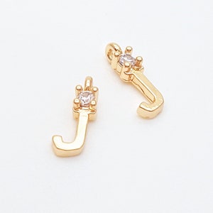 Op de afbeelding: Twee gouden letter J-bedels met een heldere strass-accent. De bedels zijn perfect om een ​​persoonlijke touch toe te voegen aan sieradenprojecten.