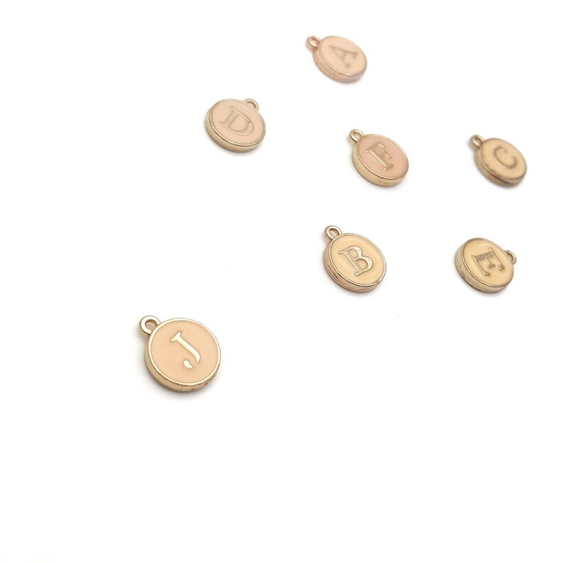 May include: A set of gold-toned metal charms with letters A, B, C, D, E, J. Each charm is a round disc with a white enamel background and a gold letter.