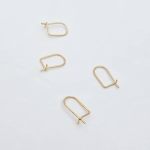 Puede incluir: Cuatro ganchos dorados para pendientes, cada uno con una parte superior curvada y una parte inferior recta con un pequeño poste. Los ganchos están dispuestos sobre una superficie blanca, mostrando su diseño simple y elegante. Ideales para la fabricación de joyas.