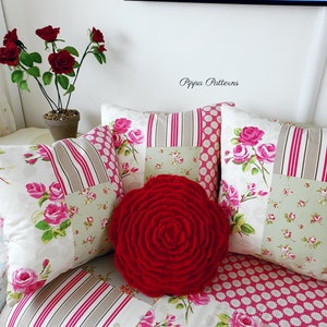 May include: A red, crocheted rose pillow sits on a couch with floral patterned cushions. The couch is covered in a patchwork fabric with pink and white stripes. The text "Pippa Patterns" is visible in the background.