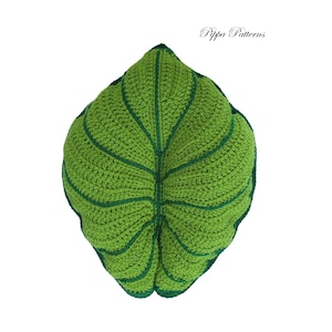 May include: A green crocheted leaf pillow with a dark green outline. The pillow is shaped like a large leaf with a central vein and smaller veins branching out.