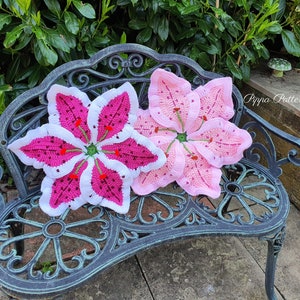 May include: Two crocheted lily flower cushions in pink and white on a black metal bench. The cushions are handmade and feature a detailed design.