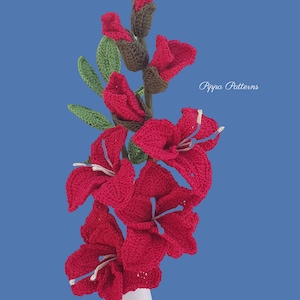 May include: A bouquet of crocheted red gladiolus flowers in a white vase. The flowers are arranged in a vase on a blue background. The text "Pippa Patterns" is visible in the upper right corner of the image.