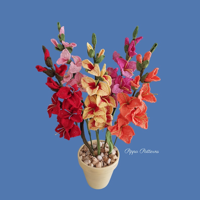 May include: A bouquet of crocheted gladiolus flowers in a variety of colors, including red, orange, yellow, pink, and white. The flowers are arranged in a terracotta pot with white stones.