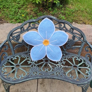 May include: A light blue crocheted flower cushion with a yellow center, sitting on a black metal bench.