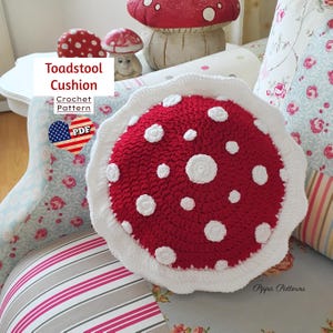 May include: A crochet toadstool cushion pattern in red and white. The pattern is available as a PDF download. The cushion is sitting on a couch with a floral pattern.