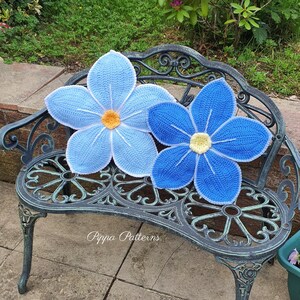 May include: Two crocheted blue flower cushions with yellow centers, sitting on a black metal garden bench. The bench is on a stone patio.