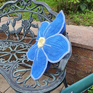 May include: A crocheted blue flower pillow with a white center and white edging. The pillow is sitting on a black metal bench.