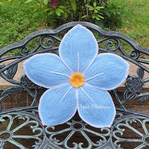 May include: A crocheted blue flower cushion with a yellow center, resting on a black metal garden bench.