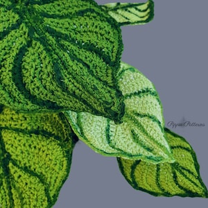 May include: Close-up of a crocheted green leaf plant with a textured surface. The leaves are layered on top of each other and have a light green and dark green color variation. The text "Pippa Patterns" is visible in the bottom right corner of the image.