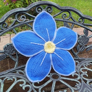 May include: A crocheted blue flower cushion with a white center. The cushion is sitting on a black metal bench.