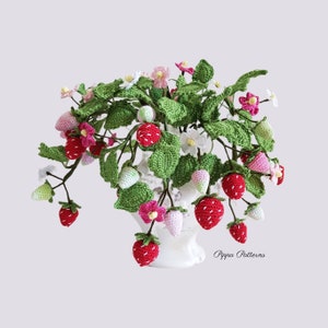 May include: A crocheted strawberry plant with red and white strawberries, green leaves, and pink and white flowers in a white vase. The plant is on a white background. The text "Pippa Patterns" is visible in the bottom right corner of the image.