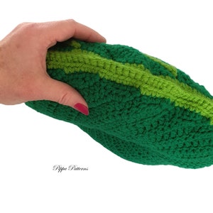 May include: A green crocheted pillow shaped like a cucumber. The pillow has a light green stripe running down the center.