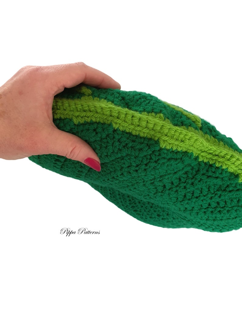 May include: A green crocheted pillow shaped like a cucumber. The pillow has a light green stripe running down the center.