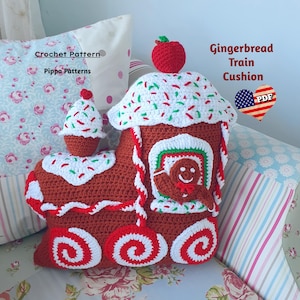 Puede incluir: Cojín de tren de jengibre tejido a crochet con un diseño de bastón de caramelo rojo y blanco. El cojín tiene forma de tren con una casa de jengibre en la parte superior. El tren tiene ruedas con diseños de bastón de caramelo rojo y blanco. La casa de jengibre tiene un techo de bastón de caramelo rojo y blanco y un hombre de jengibre en la ventana. El cojín está hecho por Pippa Patterns. Patrón de crochet PDF.