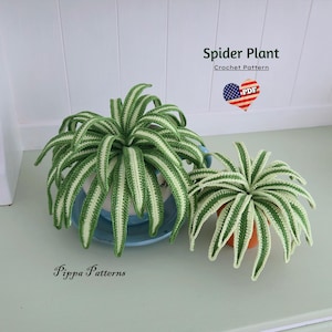 May include: Two crocheted spider plants, one large and one small, are displayed. The plants feature green and white striped leaves. The larger plant is in a blue pot, and the smaller one is in an orange pot. Text reads "Spider Plant Crochet Pattern".