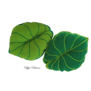 May include: Two crocheted leaf-shaped pillows in shades of green. The pillows are made with a textured stitch and have a realistic leaf design.