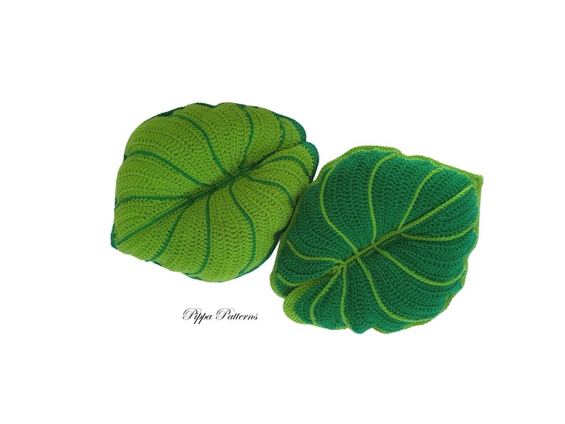 May include: Two crocheted leaf-shaped pillows in shades of green. The pillows are made with a textured stitch and have a realistic leaf design.