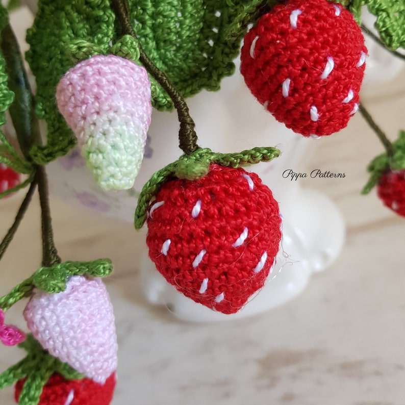 May include: A close-up of a crocheted strawberry bouquet. The strawberries are red with white stitching and green leaves. The bouquet is in a white vase. The text "Pippa Patterns" is visible in the background.