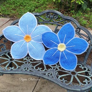 May include: Two crocheted blue flower cushions with white edging, sitting on a black metal bench. The flowers have yellow centers and are arranged in a symmetrical pattern.