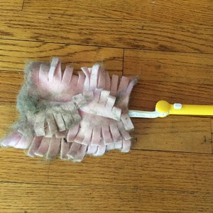 May include: A pink and yellow dust mop with a long handle. The mop head is covered in a thick layer of dust and pet hair.