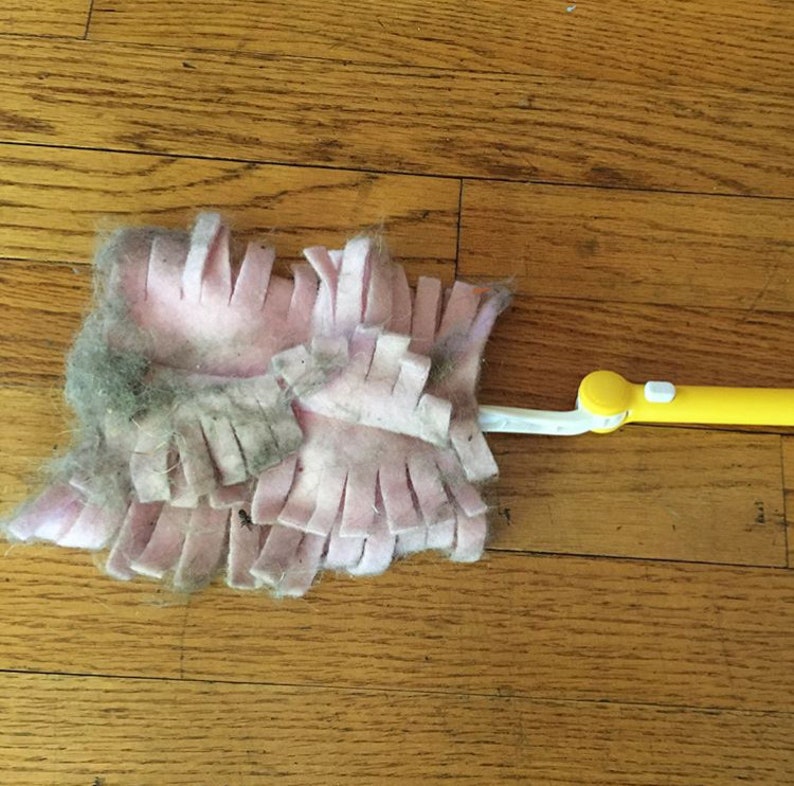 May include: A pink and yellow dust mop with a long handle. The mop head is covered in a thick layer of dust and pet hair.