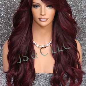Puede incluir: Una peluca larga y ondulada de color burdeos con raya lateral y flequillo. La peluca está peinada en ondas sueltas y cae hasta los hombros. La peluca está hecha de cabello sintético y está diseñada para tener un aspecto natural.