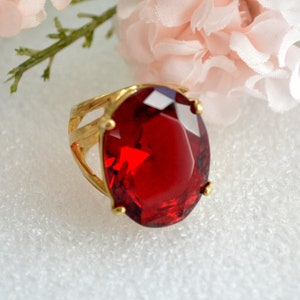 May include: A gold ring with a large, oval-shaped, red gemstone.