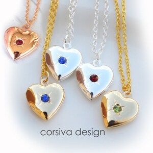 May include: Heart-shaped lockets in gold, silver, and rose gold, each with a gemstone accent. The lockets hang on delicate chains. The image includes the text "corsiva design".