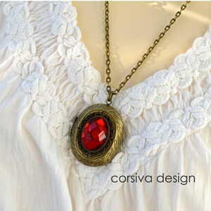 Könnte beinhalten: Eine goldene Halskette mit einem roten Edelstein-Anhänger. Das Medaillon hat ein verziertes Design und hängt an einer Kette.