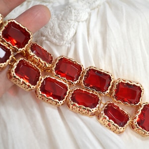 May include: A gold chain necklace with large, red, faceted, rectangular stones set in ornate gold frames.